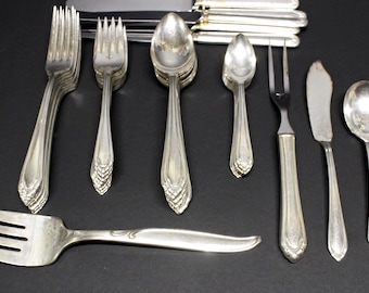 May include: A collection of antique silverware, including forks, spoons, knives, and serving utensils. The silver-colored flatware is arranged on a dark surface, showcasing the intricate designs and patterns on the handles. A classic set for dining.