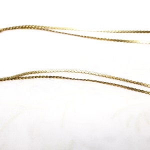 May include: A close-up shot of two delicate gold necklaces. The necklaces are made of thin, flat, circular links that catch the light. The chains are displayed against a white background, highlighting their intricate design and warm color.