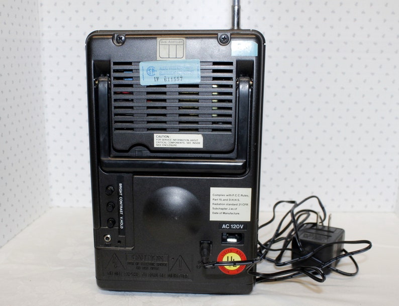 May include: Black and silver portable television with a built-in antenna, a power cord, and a label that reads "AC 120V".