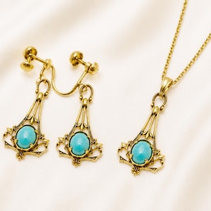 May include: A gold-toned jewelry set featuring a necklace and clip-on earrings. Each piece has a filigree design and a central oval turquoise stone. The set is displayed on a white, textured surface.