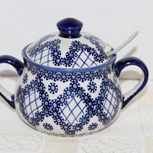 May include: A blue and white ceramic sugar bowl with a lid and a spoon. The bowl features a floral pattern with green accents.