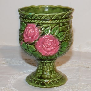 May include: A green ceramic planter with a pedestal base. The planter is decorated with pink roses and green leaves. The planter has a woven basket design.