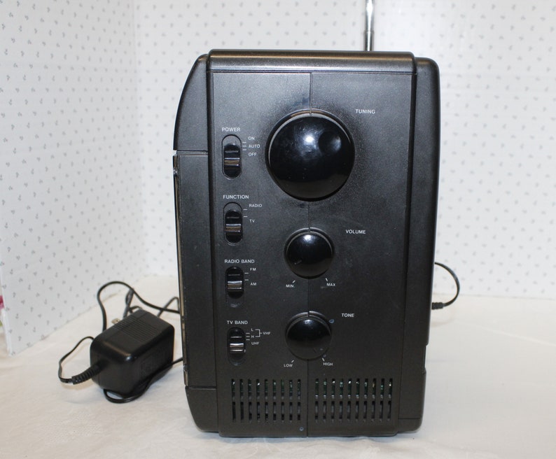 May include: Black radio with a silver antenna, multiple knobs and buttons, and a power cord. The radio has labels for "Power", "Function", "Radio Band", "TV Band", "Tuning", "Volume", and "Tone".