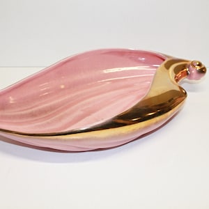 May include: A pink ceramic leaf-shaped serving dish with a gold rim and a gold handle.