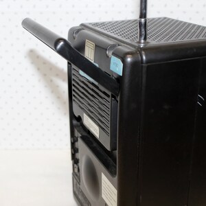 May include: A black portable radio with a built-in handle and a telescopic antenna. The radio has a speaker grill on the front and a small display on the top.