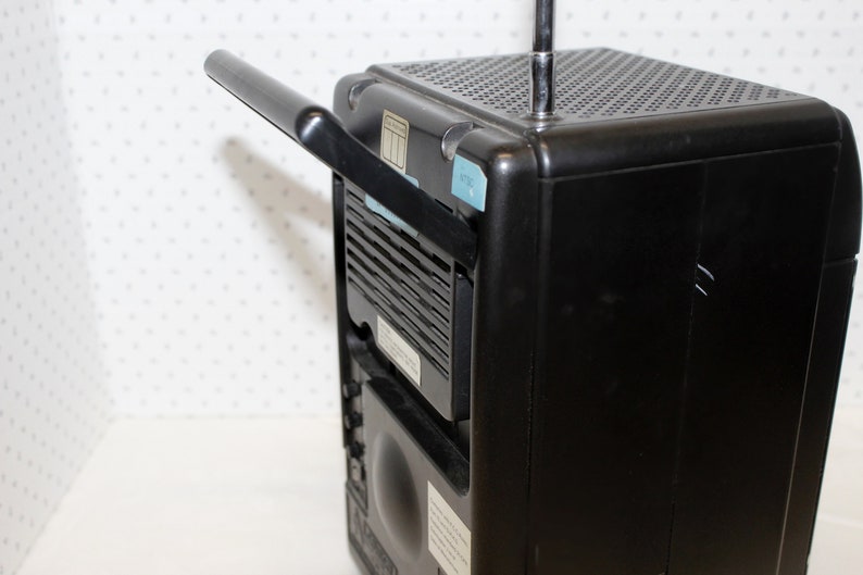 May include: A black portable radio with a built-in handle and a telescopic antenna. The radio has a speaker grill on the front and a small display on the top.