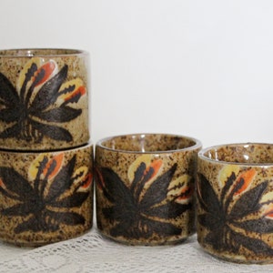 May include: Set of four brown ceramic cups with a floral design in shades of orange, yellow, and black.