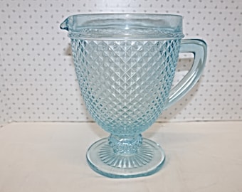 May include: A light blue glass pitcher with a diamond pattern and a pedestal base.