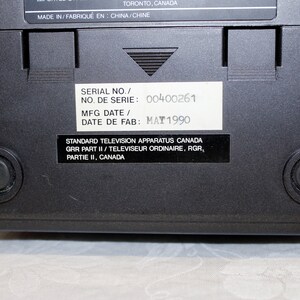 May include: Black television with a white label on the back. The label has the text "SERIAL NO./ NO. DE SERIE: 00400261 MFG DATE/ DATE DE FAB: MAY 1990 STANDARD TELEVISION APPARATUS CANADA GRR PART II/ TELEVISEUR ORDINAIRE, RGR, PARTIE II, CANADA".