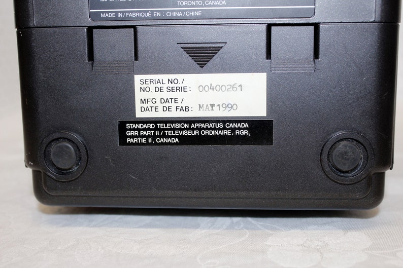 May include: Black television with a white label on the back. The label has the text "SERIAL NO./ NO. DE SERIE: 00400261 MFG DATE/ DATE DE FAB: MAY 1990 STANDARD TELEVISION APPARATUS CANADA GRR PART II/ TELEVISEUR ORDINAIRE, RGR, PARTIE II, CANADA".