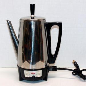 May include: A stainless steel electric percolator coffee pot with a black handle, black lid knob, and black base. The base features a label with the text REGAL, a red crown icon, and a strength selector switch labeled MILD and STRONG.