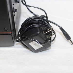 May include: Black and gray portable television with a power adapter and cord. The adapter has a label that says "12V".