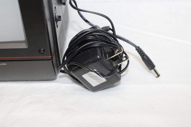 May include: Black and gray portable television with a power adapter and cord. The adapter has a label that says "12V".