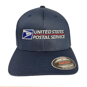 May include: A navy blue baseball cap featuring the embroidered United States Postal Service logo in white, blue, and red on the front. A circular sticker on the brim displays the text The Original Flexfit L/XL It Fits Your Life.