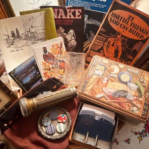 May include: A collection of vintage items including a Basic Wiring Techniques book, a 21 Useful Things You Can Build book, a Snake book, a glass mug, a metal flashlight, a Rolodex card file, a tin box with a golf scene, and small patterned buttons.