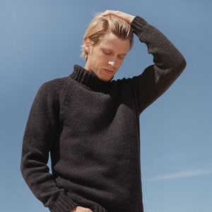 Peut inclure: Un homme portant un pull à col roulé gris foncé à texture côtelée et un jean noir. Il est debout devant un ciel bleu.