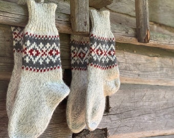 Puede incluir: Dos pares de calcetines de lana tejidos con un patrón geométrico en tonos grises, rojos y blancos colgados en un estante de madera.