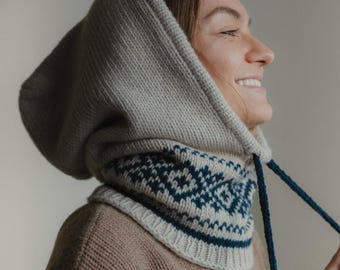 May include: A knitted hood and cowl set in neutral tones. The hood is a light gray color, with a cowl featuring a geometric pattern in navy blue and white. The cowl has a drawstring. The set is made of a soft, warm material.