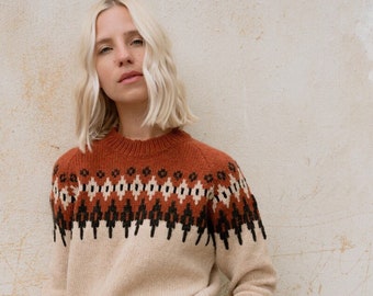 Puede incluir: Un suéter de color crema con un diseño estampado en marrón, negro y crema en el cuello. El suéter tiene mangas largas y un corte holgado.