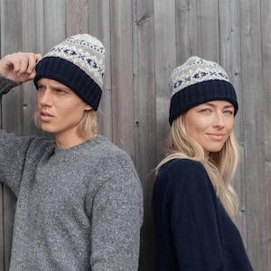 May include: Two people wearing gray and navy blue sweaters with matching patterned knit hats. The hats have a white and gray geometric pattern with a navy blue band.