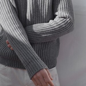 May include: A gray ribbed knit sweater with long sleeves. The sweater is folded at the elbow and the sleeves are rolled up.