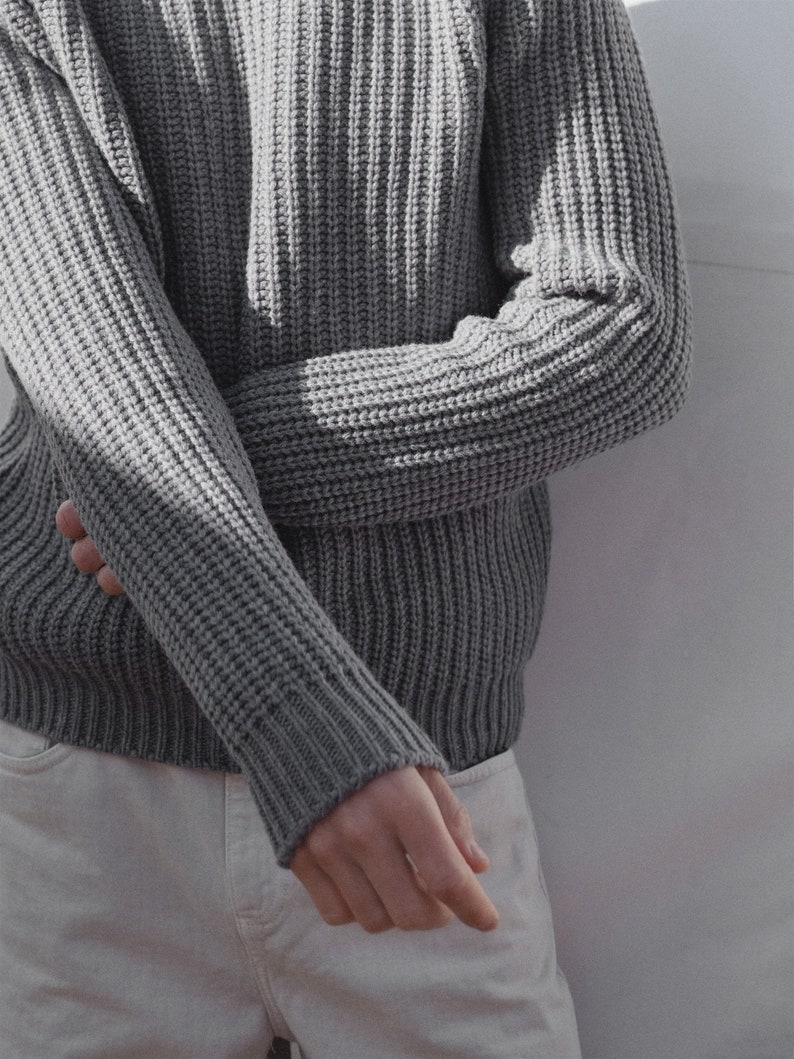 May include: A gray ribbed knit sweater with long sleeves. The sweater is folded at the elbow and the sleeves are rolled up.