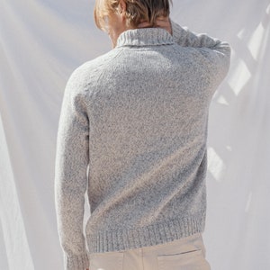 Puede incluir: Un su&eacute;ter de punto gris moteado con cuello alto y mangas largas. El su&eacute;ter lo lleva una persona con el pelo rubio.