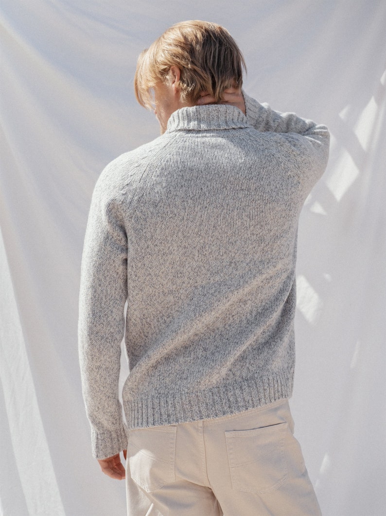 Puede incluir: Un su&eacute;ter de punto gris moteado con cuello alto y mangas largas. El su&eacute;ter lo lleva una persona con el pelo rubio.