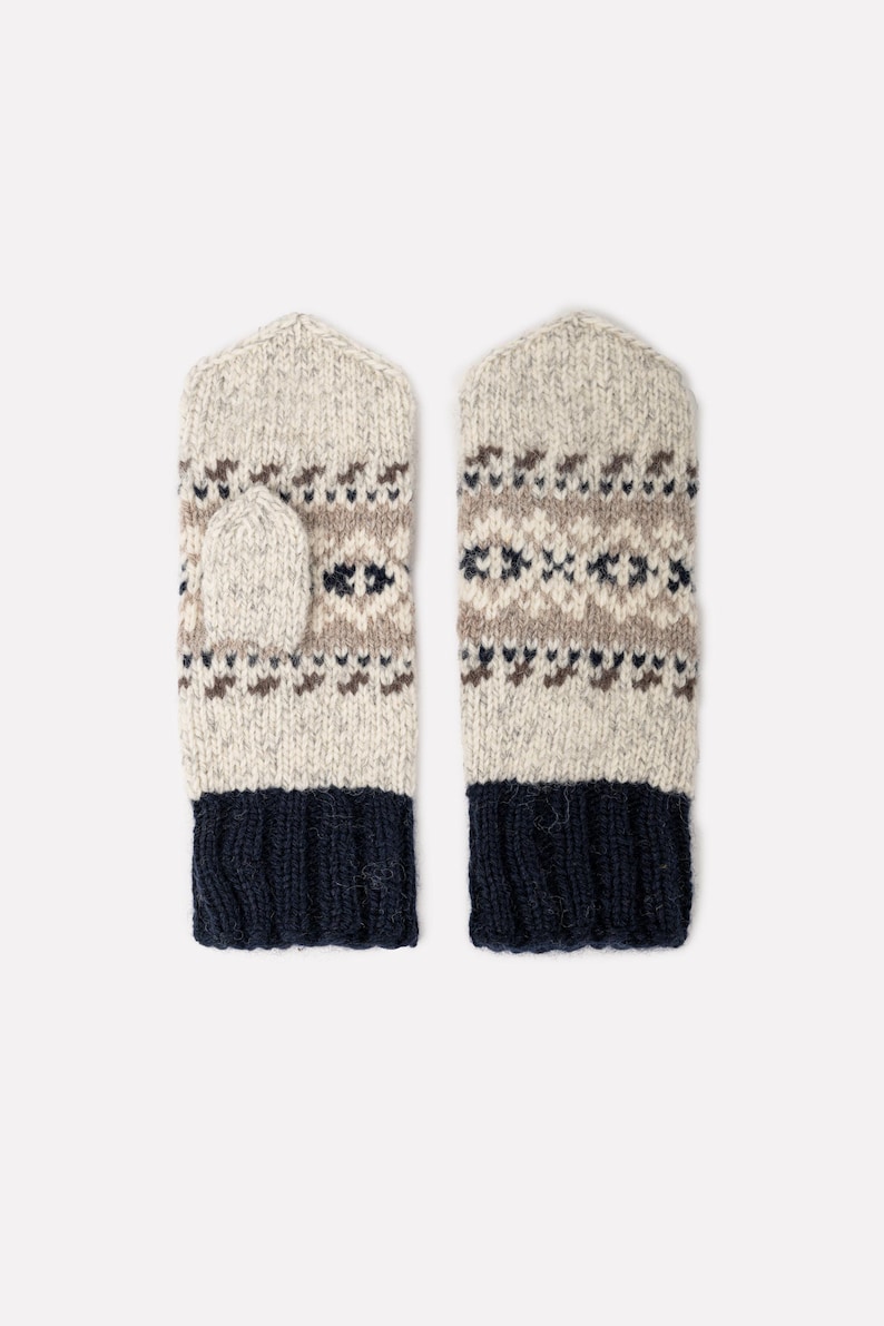 May include: A pair of knitted mittens in a neutral color palette. The mittens feature a fair isle pattern in brown and navy blue, with a navy blue cuff. The mittens are designed for warmth and style.