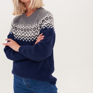 May include: A navy blue sweater with a grey and white geometric pattern. The sweater has a crew neck and long sleeves.