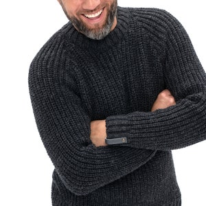 May include: A dark gray knitted sweater with a ribbed texture and a leather patch on the sleeve.