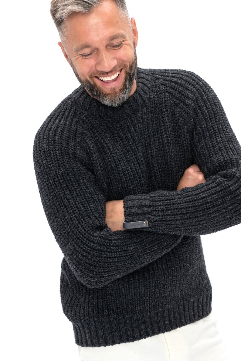 May include: A dark gray knitted sweater with a ribbed texture and a leather patch on the sleeve.