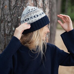 May include: A woman wearing a navy blue sweater and a knitted hat with a white and brown geometric pattern.