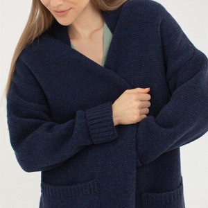 May include: A dark blue knitted cardigan with a long, open front and two patch pockets. The cardigan is made of a soft, comfortable material and has a relaxed fit.