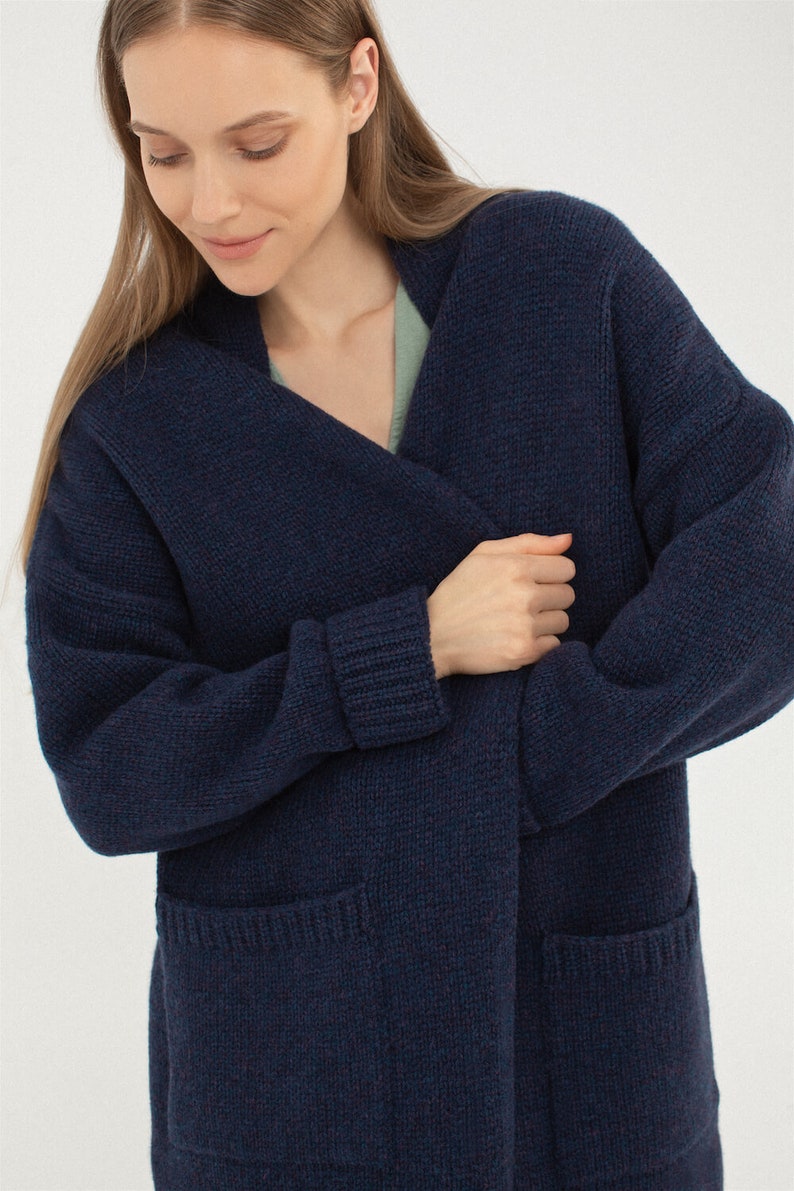 May include: A dark blue knitted cardigan with a long, open front and two patch pockets. The cardigan is made of a soft, comfortable material and has a relaxed fit.