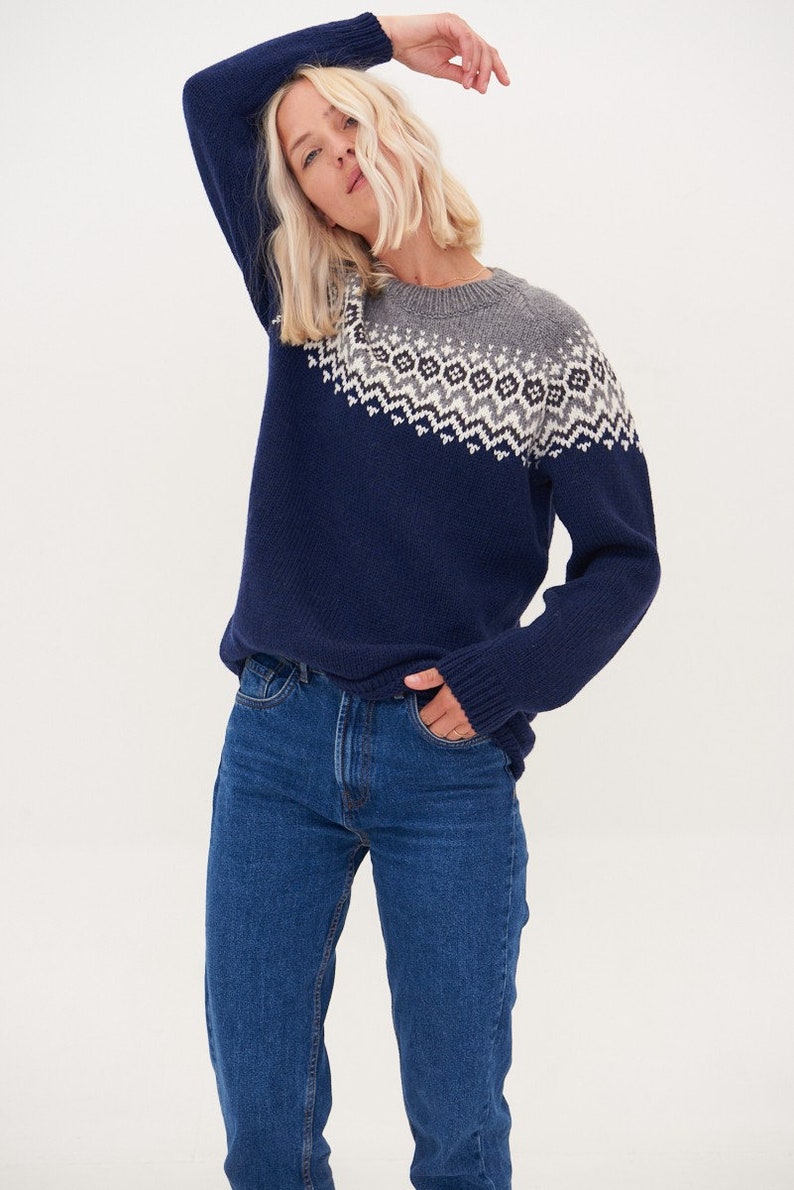 May include: A navy blue sweater with a grey and white geometric pattern on the neckline. The sweater is made of a soft, knitted fabric.