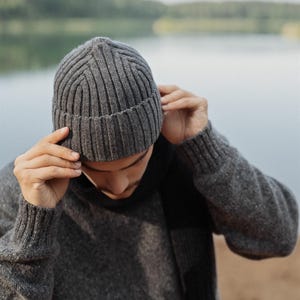 May include: A charcoal gray ribbed knit beanie hat featuring a folded cuff design. The hat is constructed with a vertical ribbed texture throughout the crown and a thicker ribbed band at the base, providing a structured fit for the head.