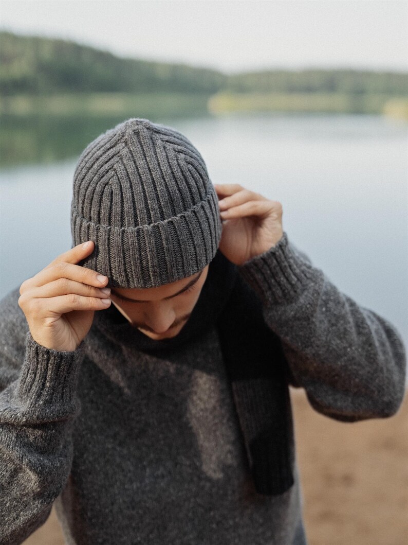 May include: A charcoal gray ribbed knit beanie hat featuring a folded cuff design. The hat is constructed with a vertical ribbed texture throughout the crown and a thicker ribbed band at the base, providing a structured fit for the head.