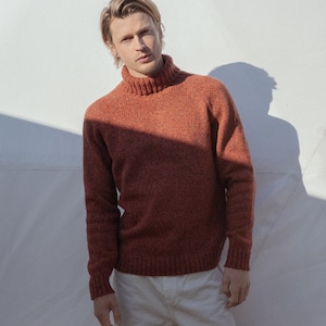 Puede incluir: Un hombre con un su&eacute;ter de cuello alto color &oacute;xido con cuello de canal&eacute; y pantalones blancos.