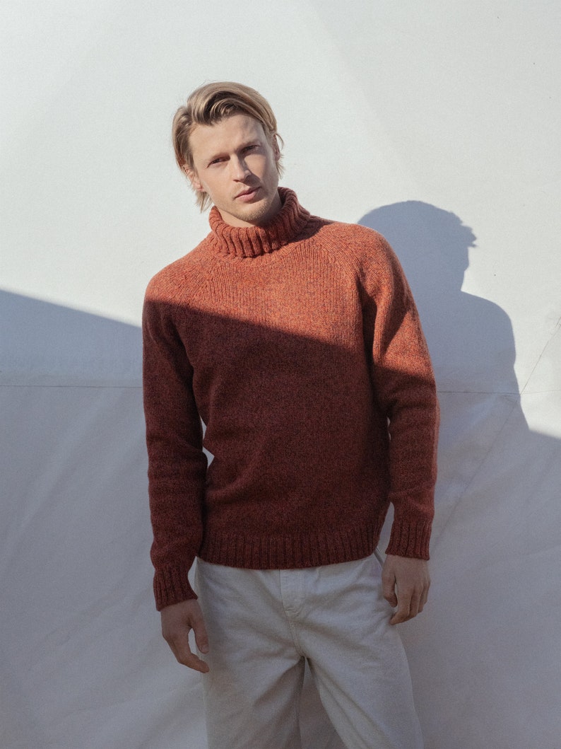 Puede incluir: Un hombre con un su&eacute;ter de cuello alto color &oacute;xido con cuello de canal&eacute; y pantalones blancos.