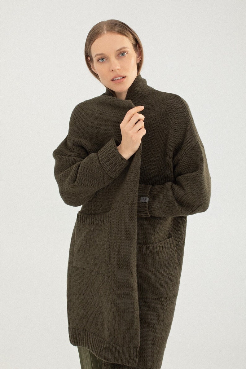 May include: A long, dark green cardigan with a shawl collar and two pockets. The cardigan is made of a soft, knitted fabric.