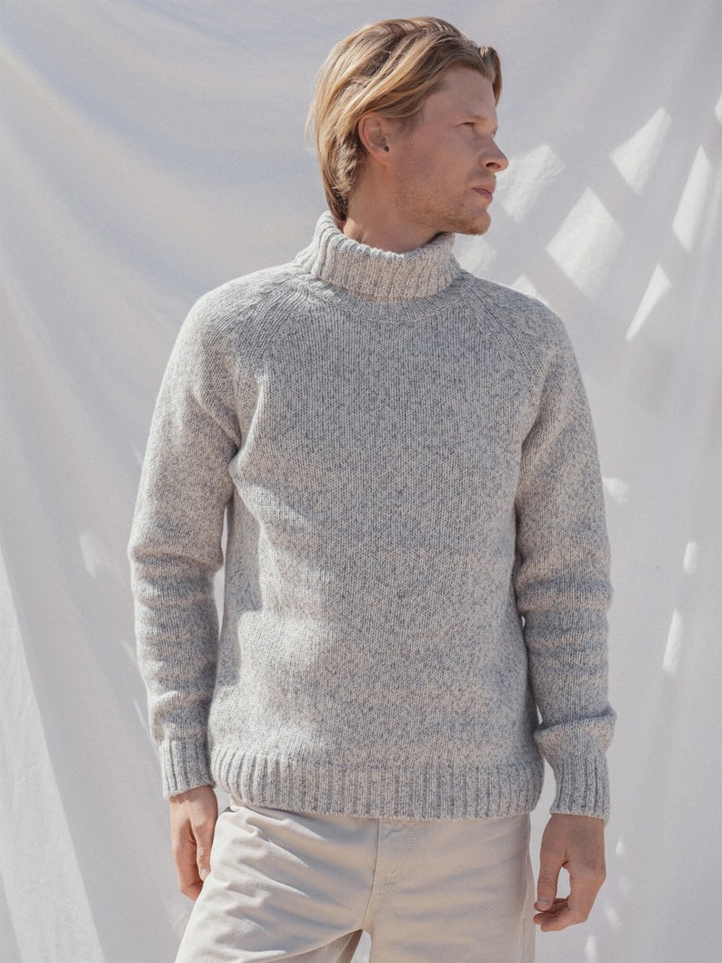 Puede incluir: Un su&eacute;ter gris de cuello alto con textura moteada. El su&eacute;ter tiene un cuello y pu&ntilde;os de canal&eacute;.