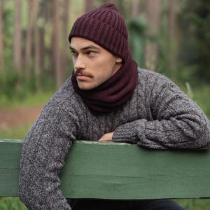 May include: A deep burgundy ribbed knit beanie and a matching burgundy neck warmer worn with a grey cable knit sweater. The beanie features a classic cuffed design, while the neck warmer provides a snug fit around the neck area.