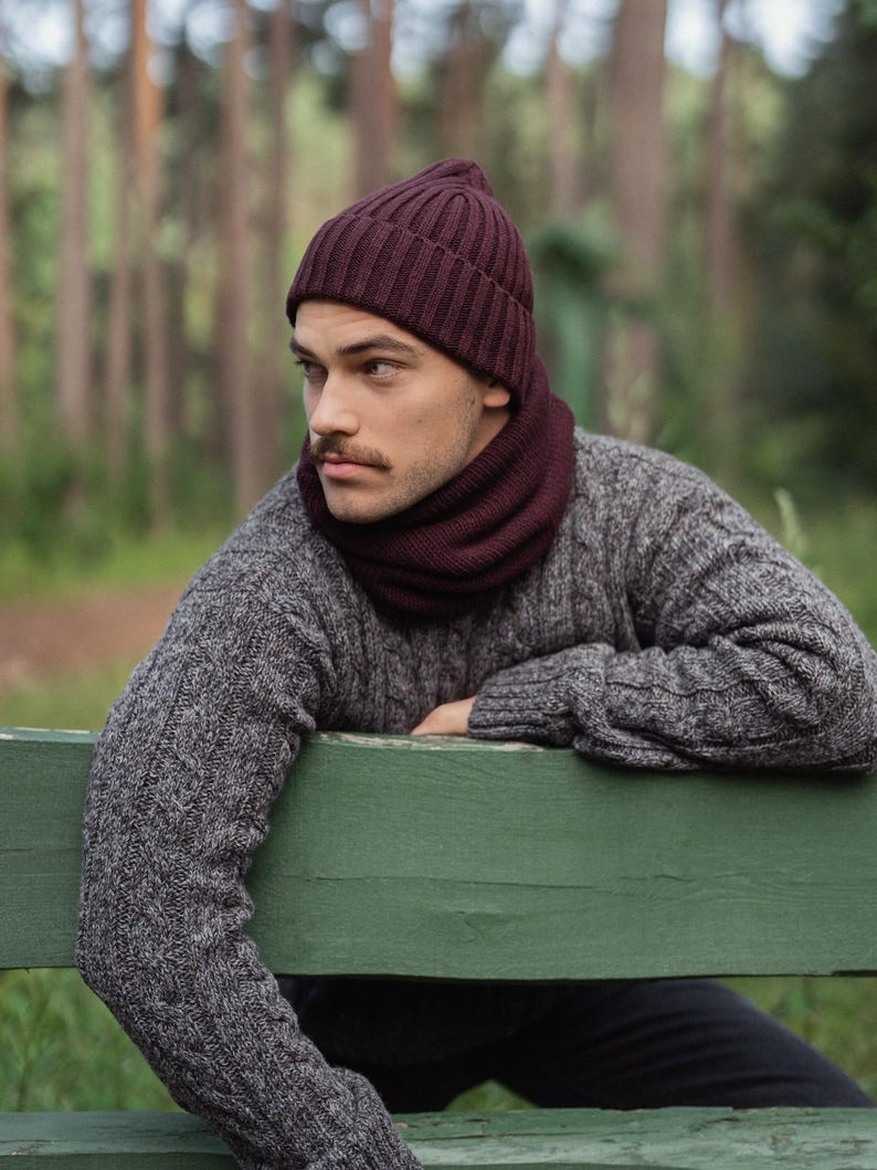 May include: A deep burgundy ribbed knit beanie and a matching burgundy neck warmer worn with a grey cable knit sweater. The beanie features a classic cuffed design, while the neck warmer provides a snug fit around the neck area.