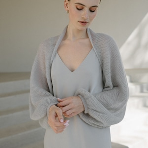May include: A light gray sleeveless dress with a V-neckline paired with a matching light gray sheer knit bolero. The bolero features long, voluminous balloon sleeves with fitted cuffs, crafted from a delicate, open-weave, semi-transparent yarn.