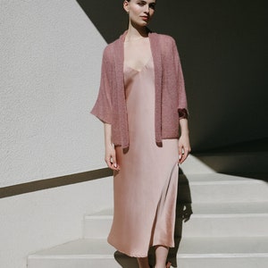 Puede incluir: Una mujer con un c&aacute;rdigan rosa empolvado sobre un vestido de sat&eacute;n rosa empolvado y zapatos de tac&oacute;n de ante marr&oacute;n. Est&aacute; de pie en una escalera.