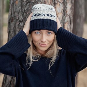 May include: A woman wearing a navy blue sweater and a knitted hat with a white and brown geometric pattern.