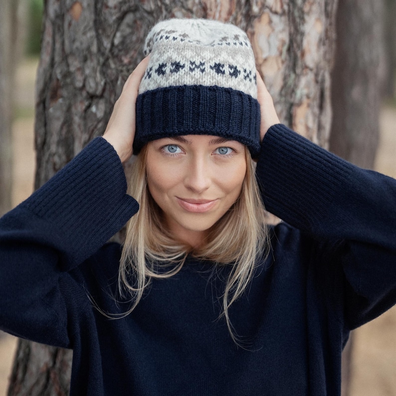 May include: A woman wearing a navy blue sweater and a knitted hat with a white and brown geometric pattern.