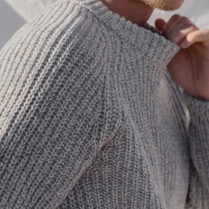 May include: A gray knitted sweater with a ribbed texture. The sweater has a crew neck and long sleeves.