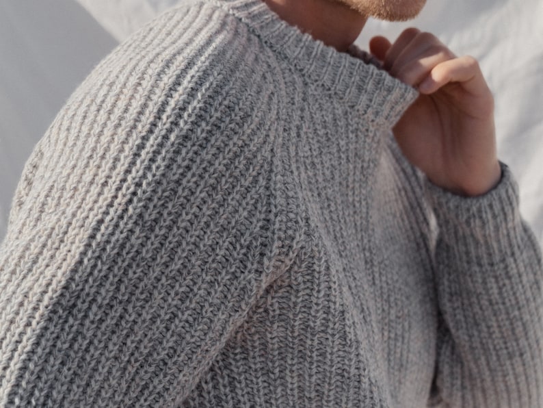 May include: A gray knitted sweater with a ribbed texture. The sweater has a crew neck and long sleeves.